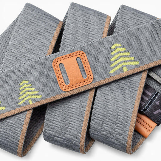 A close-up of the Arcade Belts Blackwood strap in gray fabric, showcasing subtle yellow tree accents, tan edges, and a neatly stitched orange A2 buckle—all folded with care.