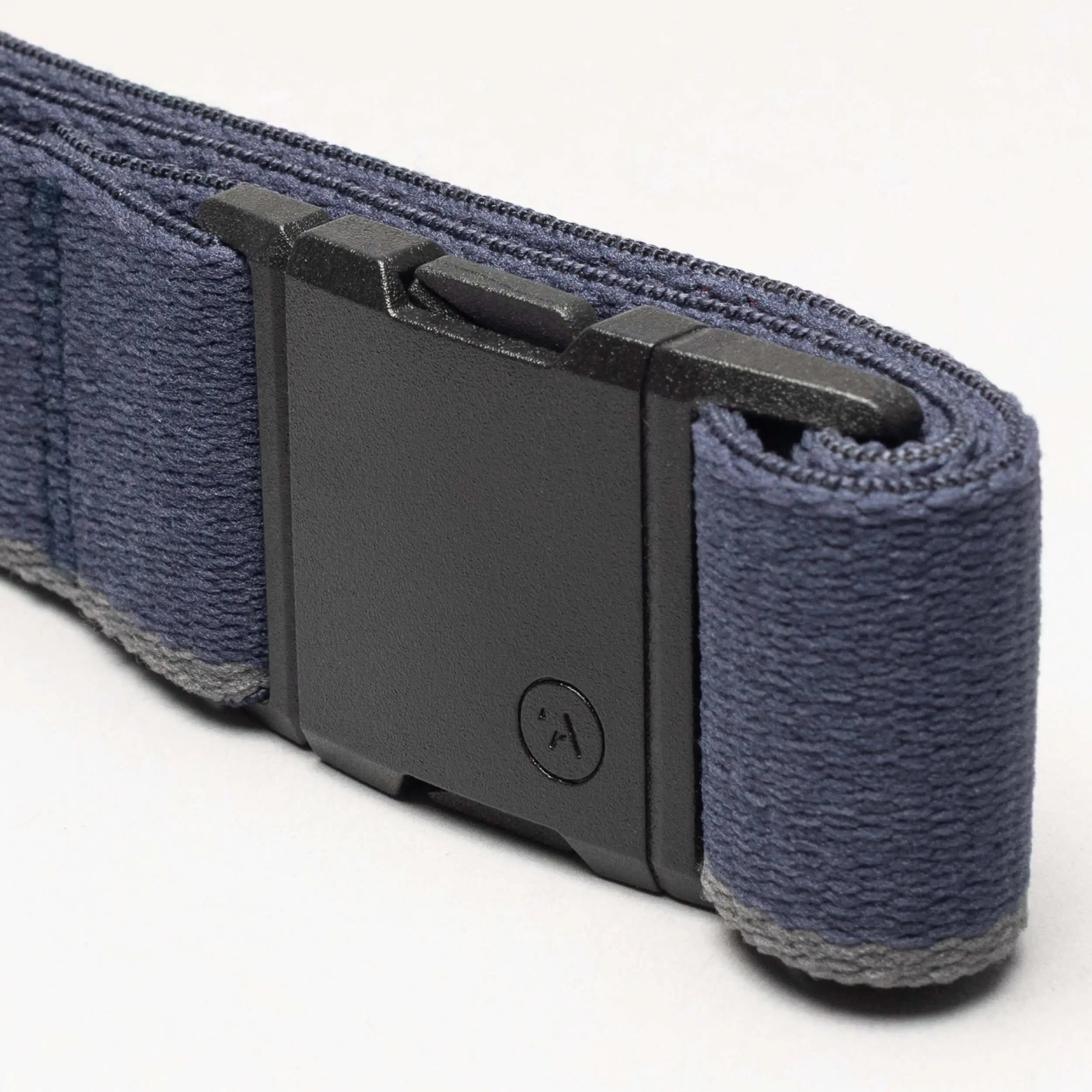 A close-up of the Blackwood belt by Arcade Belts, featuring a sleek dark blue strap and a black A2 rectangular buckle with a small circular logo, resting on a light gray surface.