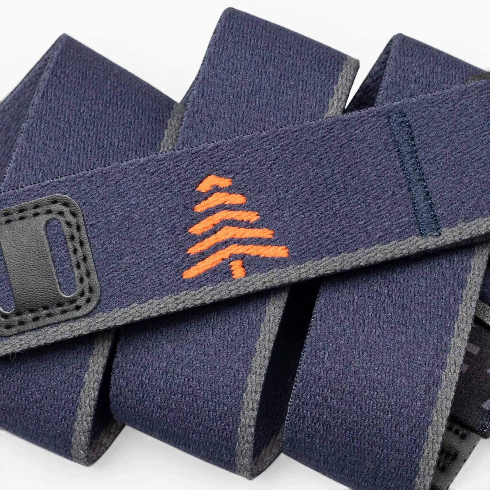 A close-up of the Arcade Belts Blackwood shows a navy blue strap with grey edges, an orange embroidered tree in the center, and black stitched accents, showcasing its stylish craftsmanship.