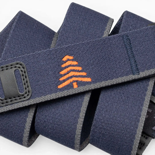 A close-up of the Arcade Belts Blackwood shows a navy blue strap with grey edges, an orange embroidered tree in the center, and black stitched accents, showcasing its stylish craftsmanship.