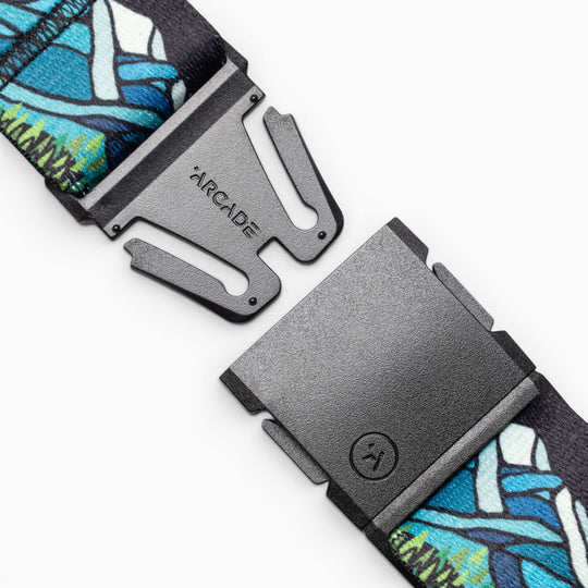 Close-up of a black Arcade Belts Broken Arrow buckle, engraved with the brand name and attached to a vibrant blue and green strap—perfect for trail running. The partially open buckle shows its unique interlocking design.