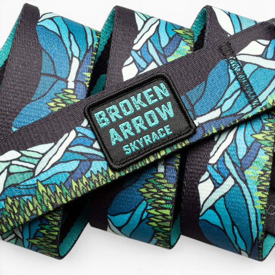 The Arcade Belts Broken Arrow features a vibrant blue, green, and white nature-inspired fabric lanyard and a patch reading BROKEN ARROW SKYRACE in bold letters—perfect for trail running enthusiasts.