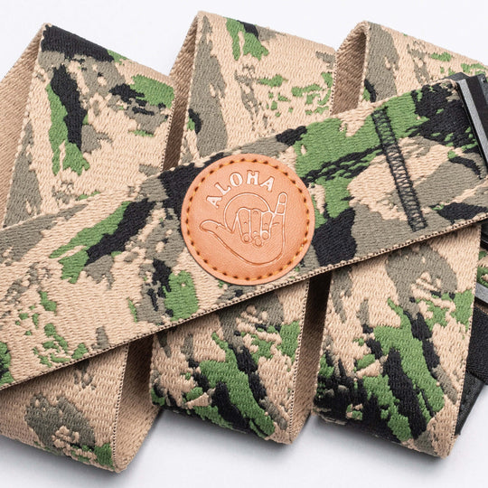 The Arcade Belts Island Collection Low Profile Belt features a camouflage pattern, round leather patch with ALOHA and shaka hand sign, black buckle, and elastic stretch for stylish comfort.