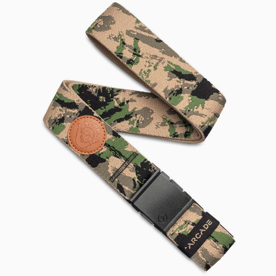 The Arcade Belts Island Collection travel belt features a green, tan, and black camo pattern, durable plastic buckle, brown leather patch, and a small Arcade Belts logo tag near the end.