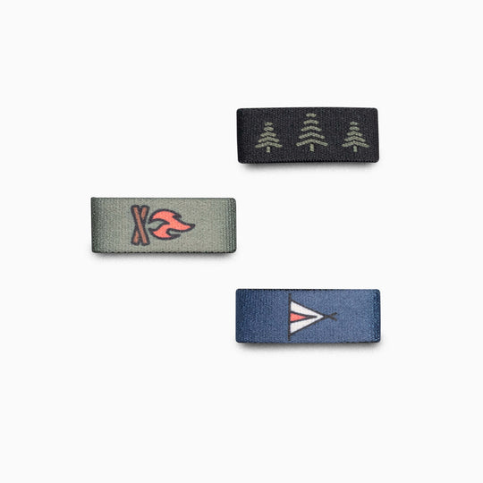 Three rectangular Belt Loopkeepers by Arcade Belts in Camp—featuring pine trees on black, a campfire on green, and a tent on blue—make perfect accents for Standard Width Adventure or Lifestyle Belts. Shown on a plain white background.