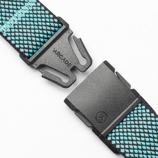A close-up of the black A2 buckle on Arcade Belts' Carry strap, featuring a blue and black crisscross pattern. The separated buckle displays 'ARCADE', highlighting performance stretch webbing for comfort and durability.