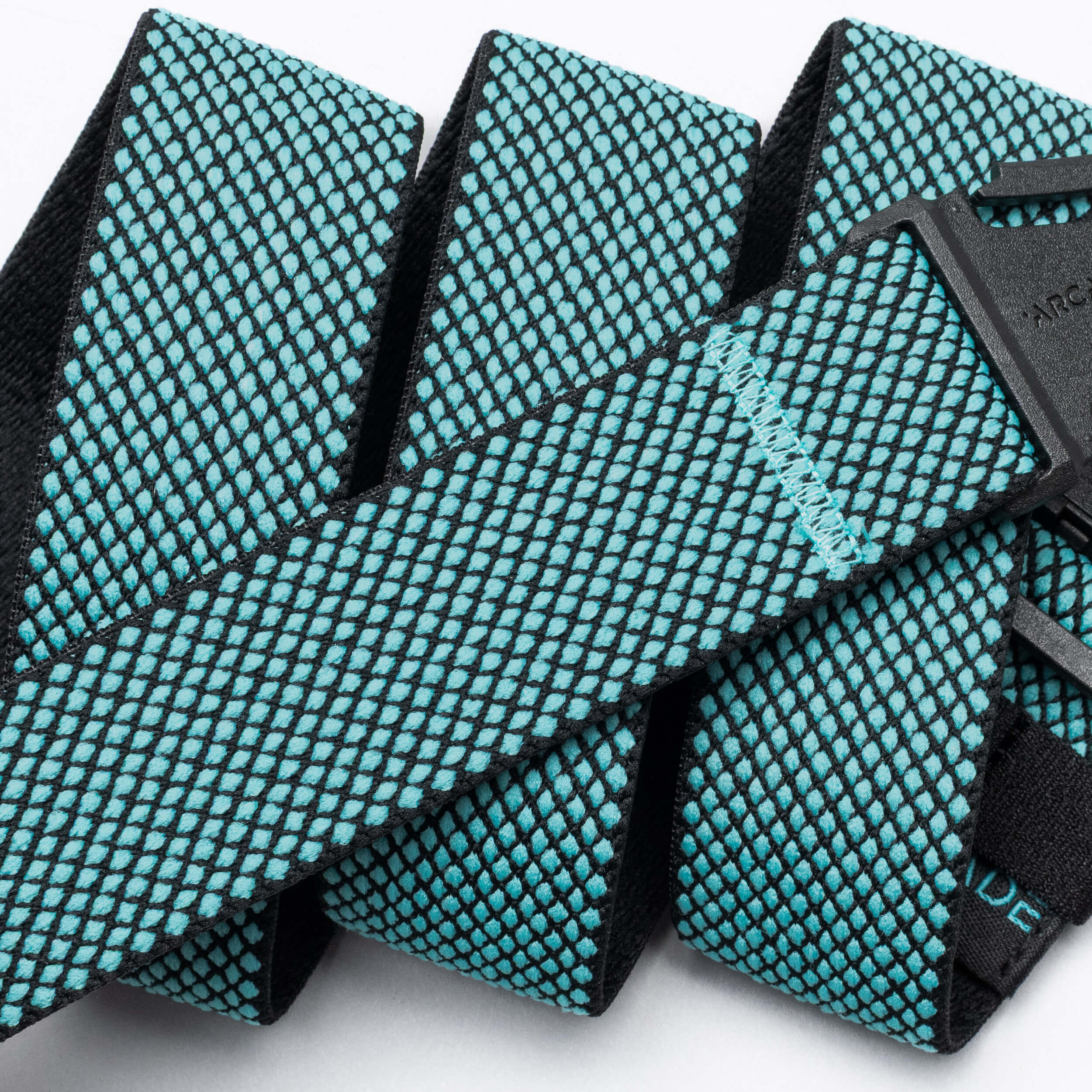A close-up of the Arcade Belts Carry: a woven fabric belt with a black base and turquoise diamond pattern, stitched details, performance stretch webbing, and a plastic buckle.
