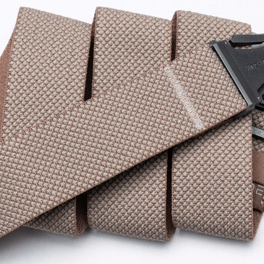 Close-up of the Arcade Belts Carry, a textured light brown woven fabric belt with a black A2 buckle, neatly folded in parallel layers against a white background.