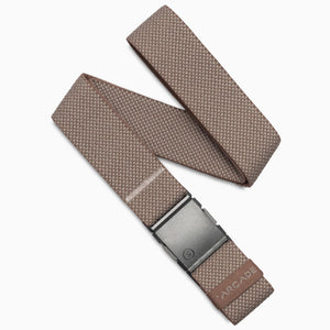 The Arcade Belts Carry is a taupe textured fabric belt with performance stretch webbing, a black rectangular buckle, and a small leather ARCADE tag near the end. It’s displayed neatly folded in a loose zigzag pattern.