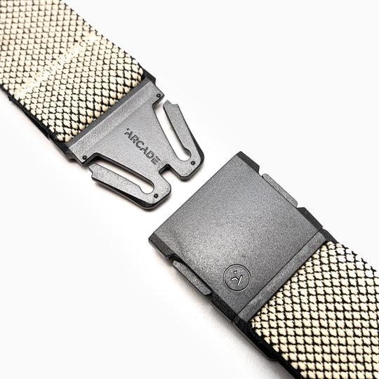 A close-up of the Arcade Belts Carry—a black and white woven belt with a black plastic A2 buckle, partially unclasped. The buckle shows the brand name and logo. Crafted from performance stretch webbing, set on a white background.