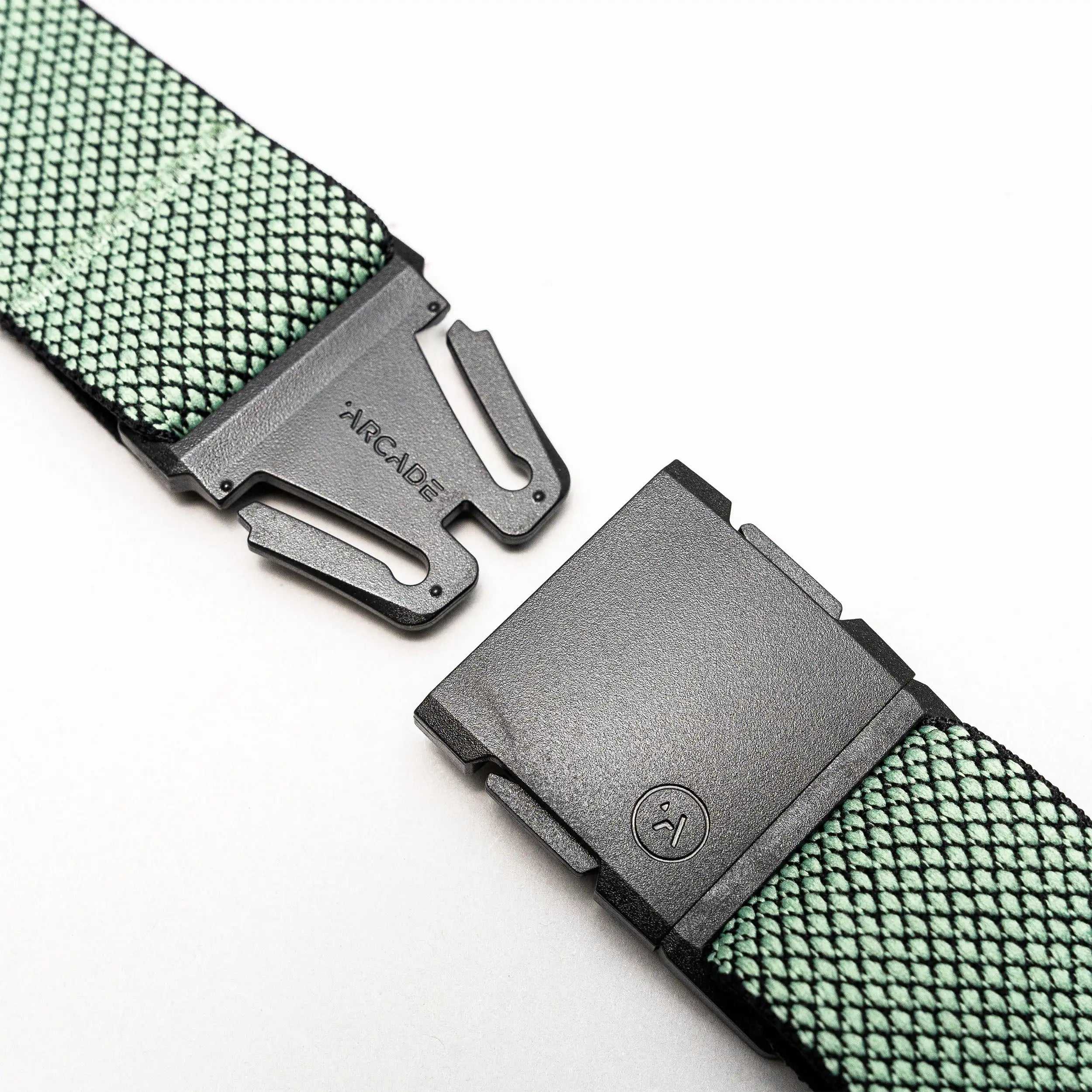 A close-up of the Arcade Belts Carry showcases its green performance stretch webbing and unique weave, featuring a black plastic A2 buckle that is partially unclasped and displays the brand name.