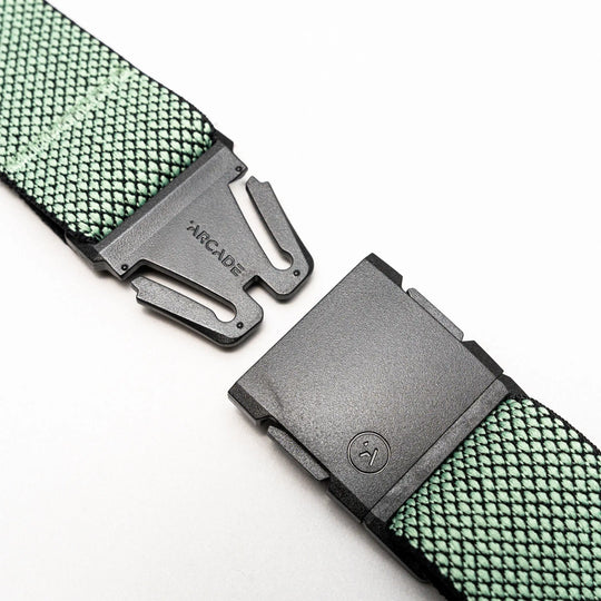 A close-up of the Arcade Belts Carry showcases its green performance stretch webbing and unique weave, featuring a black plastic A2 buckle that is partially unclasped and displays the brand name.