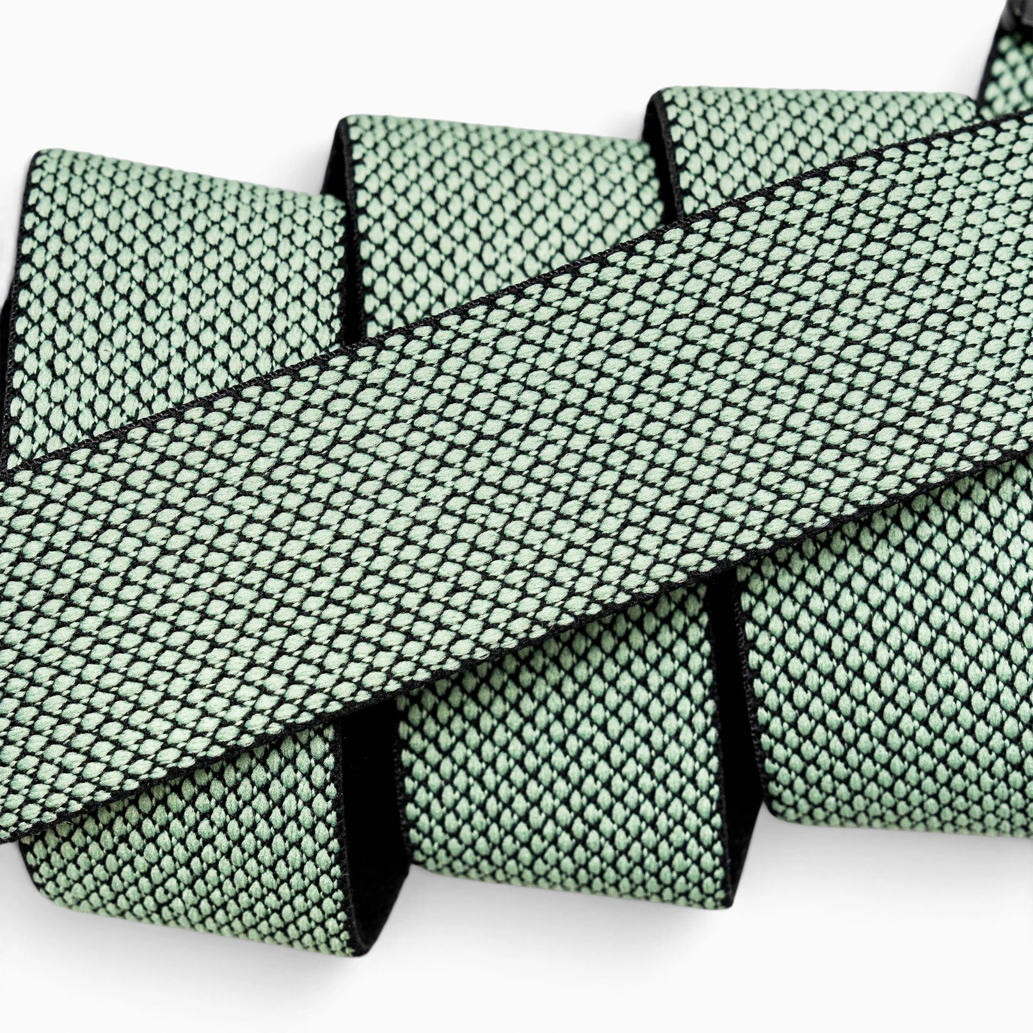 A close-up of the Arcade Belts Carry belt—a flat, mint green woven strap featuring a black diamond pattern, crafted from performance stretch webbing—looped back and forth against a white background.