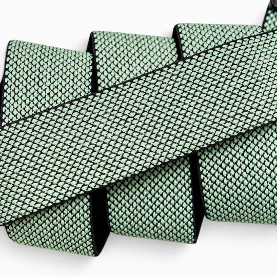 A close-up of the Arcade Belts Carry belt—a flat, mint green woven strap featuring a black diamond pattern, crafted from performance stretch webbing—looped back and forth against a white background.