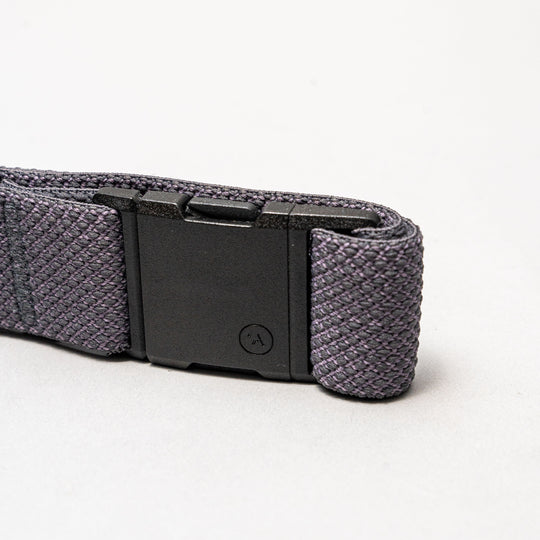 A close-up of the Arcade Belts Carry: a dark gray woven elastic stretch belt with a low-profile black rectangular plastic buckle, shown against a plain light gray background.