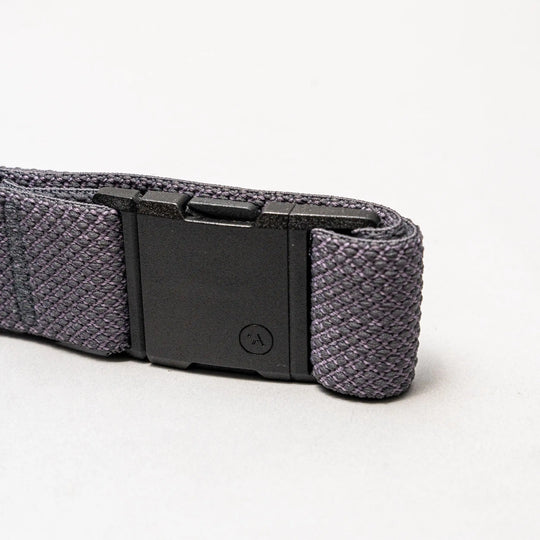 A close-up of the Arcade Belts Carry: a dark gray woven elastic stretch belt with a low-profile black rectangular plastic buckle, shown against a plain light gray background.