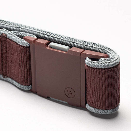 A close-up view of the Arcade Belts Carto, a maroon elastic stretch belt with gray edges and a rectangular, matte maroon buckle, shown on a light background.