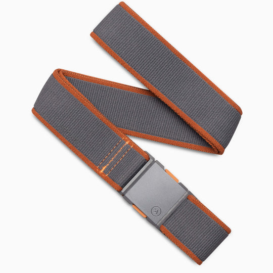The Arcade Belts Carto Kit is a gray elastic stretch belt with orange edges and stitching, featuring a matte gray plastic low-profile buckle—perfect for travel and all-day comfort. Shown laid out on a white background.