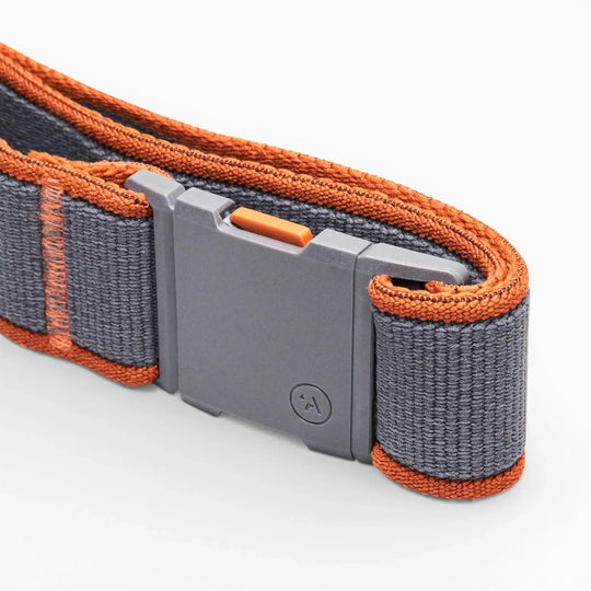 A close-up of the Arcade Belts Carto, a gray belt with orange edges and a plastic rectangular buckle featuring a small logo, set against a white background; its low profile makes it ideal for travel or everyday use.