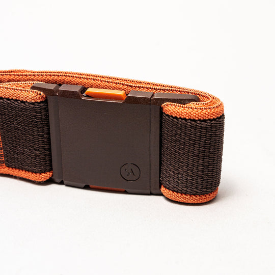 A close-up of the Arcade Belts Carto, a black and orange woven fabric low profile belt with a black rectangular plastic buckle, displayed on a plain white background.