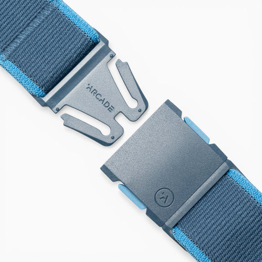 Close-up of the Carto performance stretch belt by Arcade Belts in blue, featuring light blue edge stitching for added comfort and adventure. The partially open metal clasp is engraved with “ARCADE” and displays the brand’s logo on the lower section.