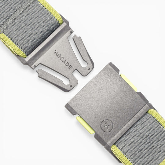 A close-up of a gray and yellow Carto performance stretch belt by Arcade Belts, featuring a metal buckle engraved with the ARCADE name and a simple smiley face logo. Designed for adventure, the belt’s detailed stitching and secure clasp are prominently displayed, highlighting the high-quality construction that sets Arcade Belts apart.