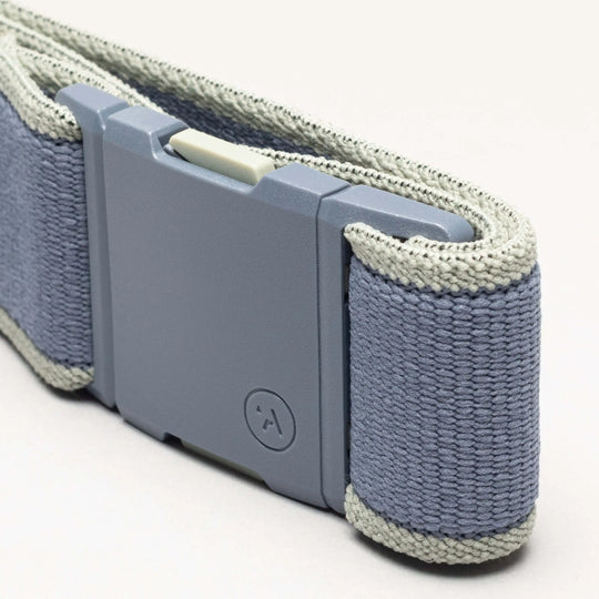 A close-up of the Carto by Arcade Belts—a gray and light blue performance stretch belt wristband with a rectangular plastic buckle and a small circular logo—shown on a plain background to highlight its adventure-ready design.