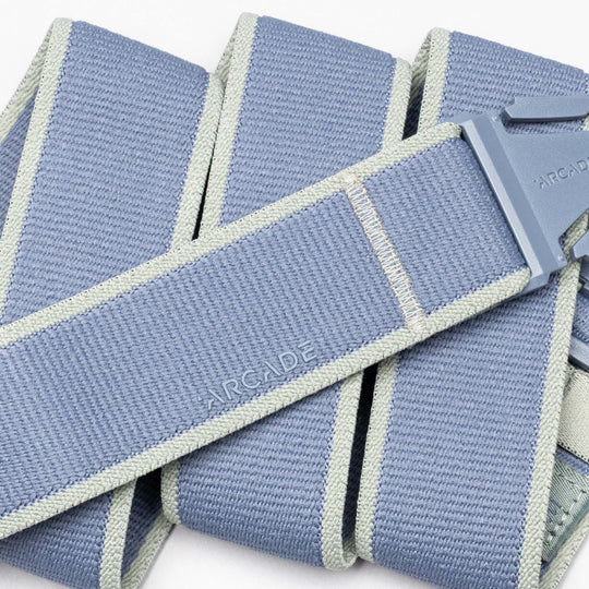 A close-up of a light blue and gray Arcade Belts Carto performance stretch belt with a plastic buckle. The belt, embossed with "ARCADE" and neatly folded, is ideal for adventure seekers.
