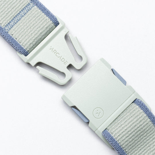 A close-up of the grey and light blue Carto performance stretch belt by Arcade Belts features a plastic buckle, partially unclasped, with "ARCADE" engraved—ready for your next adventure.