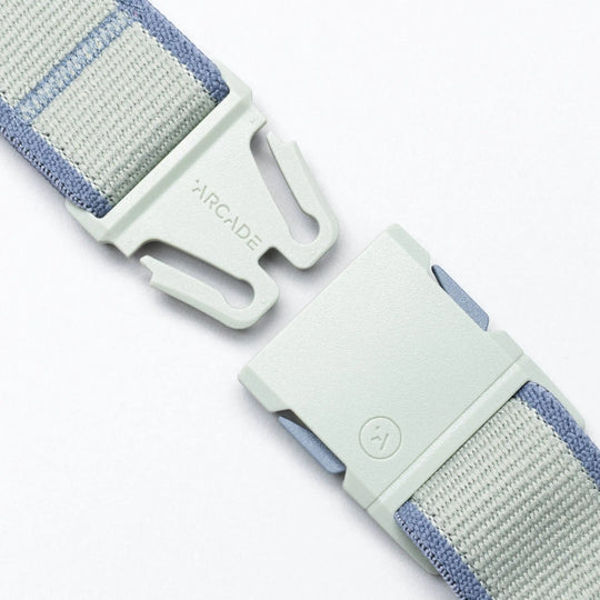 A close-up of the grey and light blue Carto performance stretch belt by Arcade Belts features a plastic buckle, partially unclasped, with "ARCADE" engraved—ready for your next adventure.