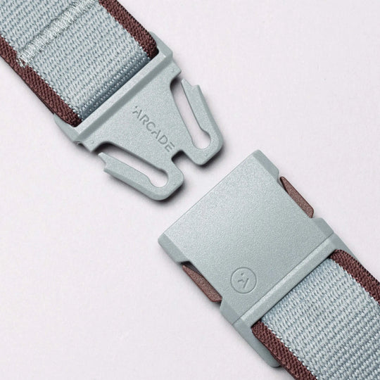 Close-up of a light gray plastic buckle on the Carto Elastic Stretch Belt by Arcade Belts, featuring brown edging, partially unfastened against a light background. The word ARCADE is printed on one side, reflecting the brands signature style.