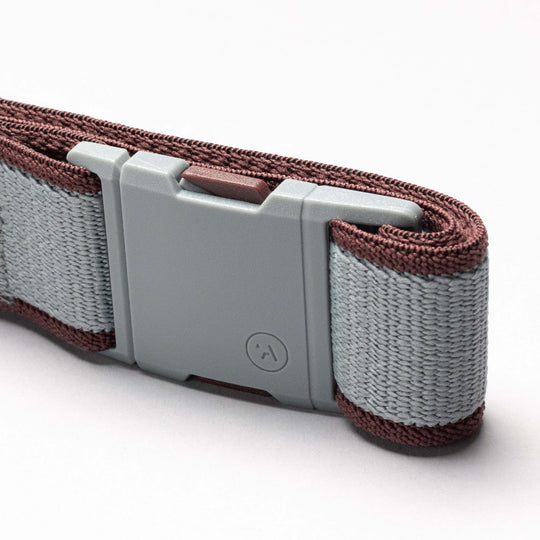A close-up of the Arcade Belts Carto, featuring a gray plastic buckle and a light gray/brown woven stretch webbing strap, neatly folded against a plain white background.
