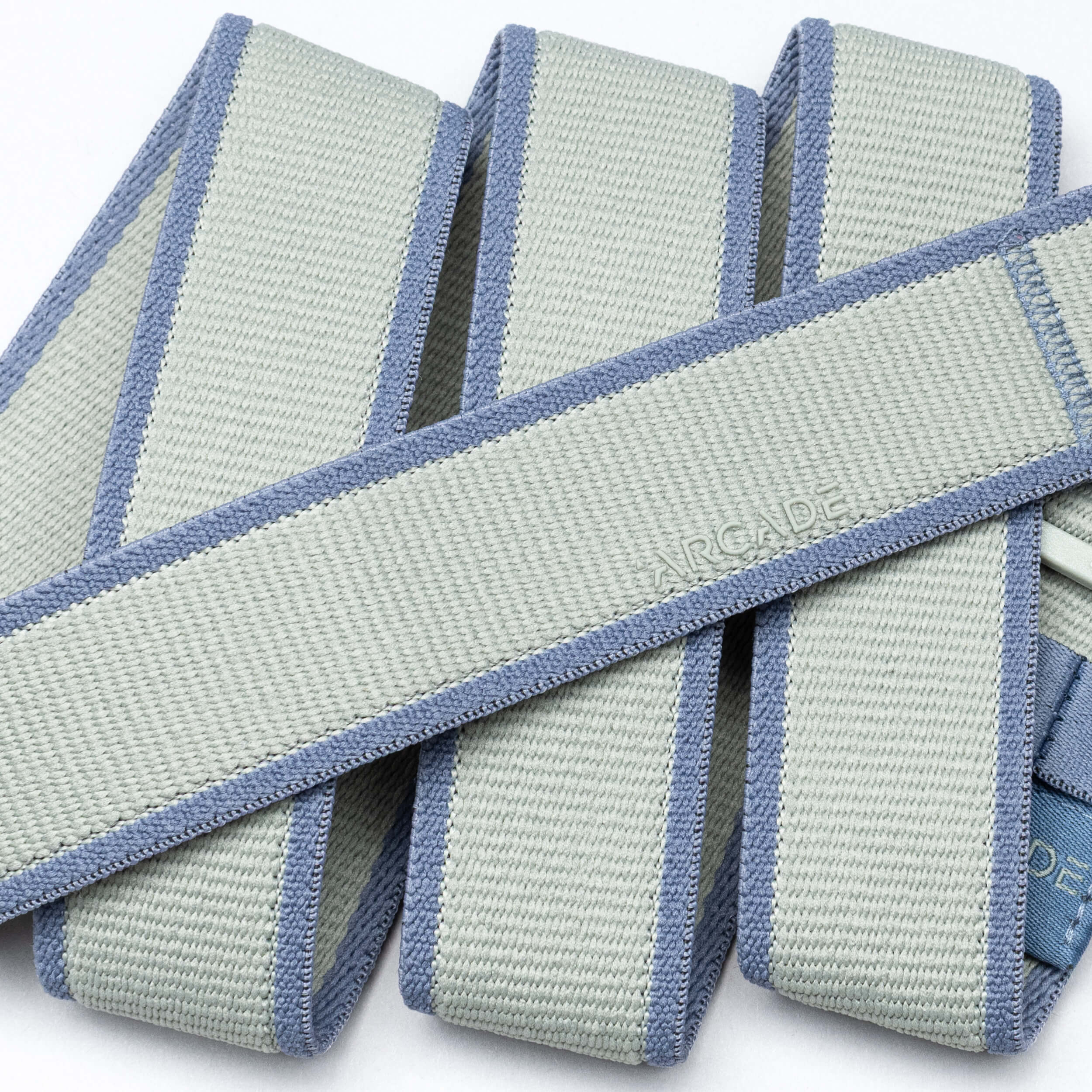 A close-up of folded grey and light blue Carto resistance bands by Arcade Belts, featuring textured material, reinforced edges, and a subtly embossed brand name that reflects the quality of their performance stretch belts.
