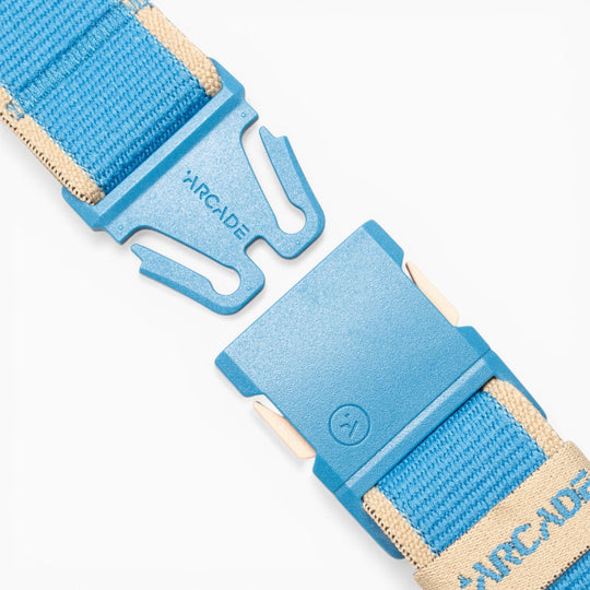 A close-up of the Carto performance stretch belt by Arcade Belts in blue and beige, featuring a blue plastic buckle, shown unfastened on a white background—ideal for adventure seekers who prioritize comfort and style.