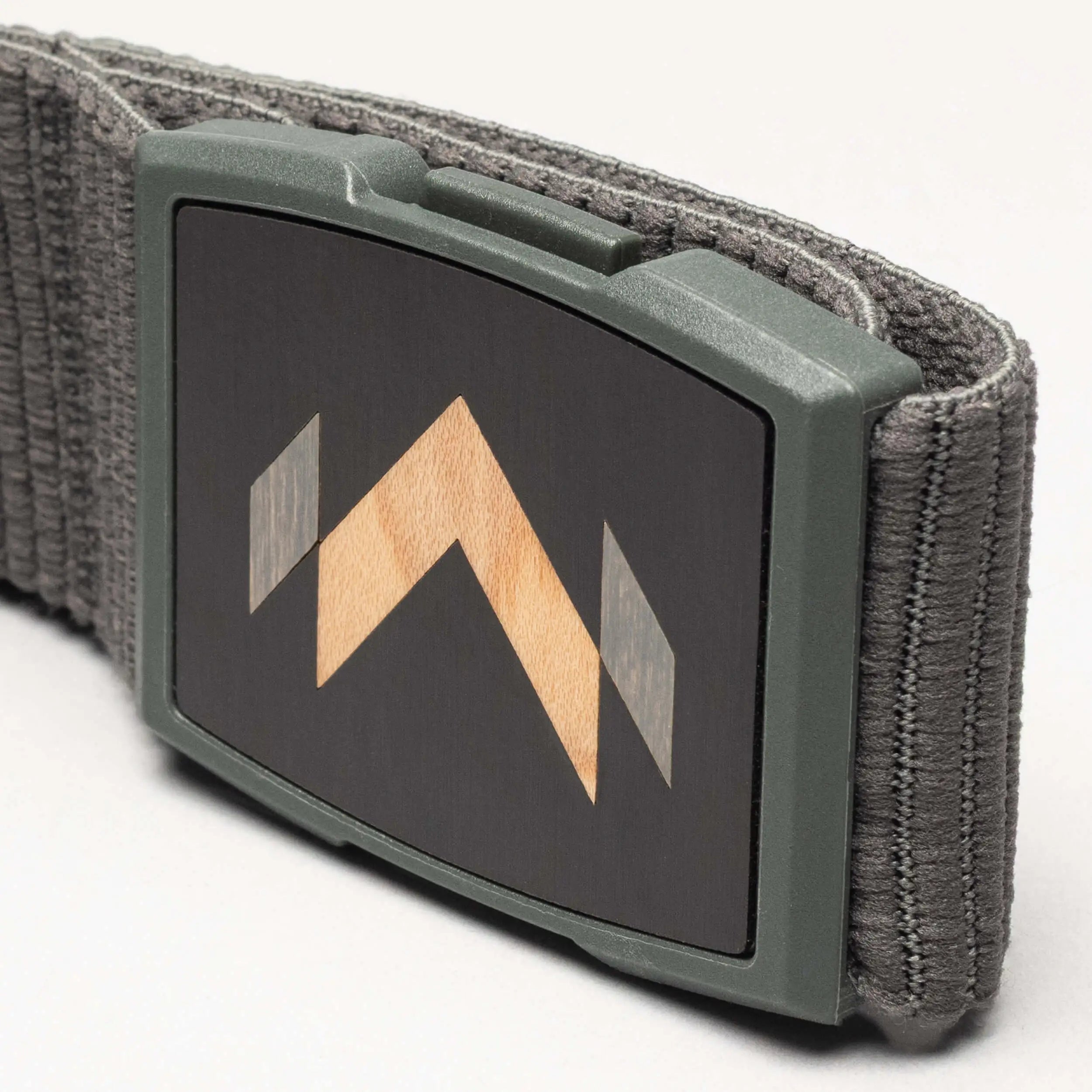 A close-up of the Arcade Belts Carver: a gray stretch belt with a rectangular buckle featuring a black face and geometric wood inlay with light and dark wood tones—a signature Carver detail.