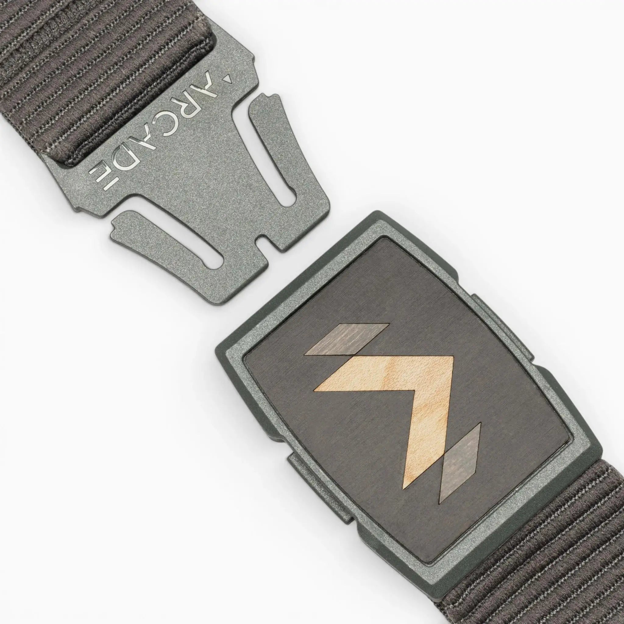 A close-up of the dark grey Carver stretch belt by Arcade Belts, featuring a partially unfastened metal buckle with geometric wood inlay and ARCADE engraved on the clasp, plus a textured strap.
