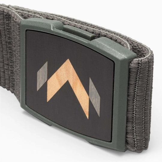 A close-up of the Arcade Belts Carver: a gray stretch belt with a rectangular buckle featuring a black face and geometric wood inlay with light and dark wood tones—a signature Carver detail.