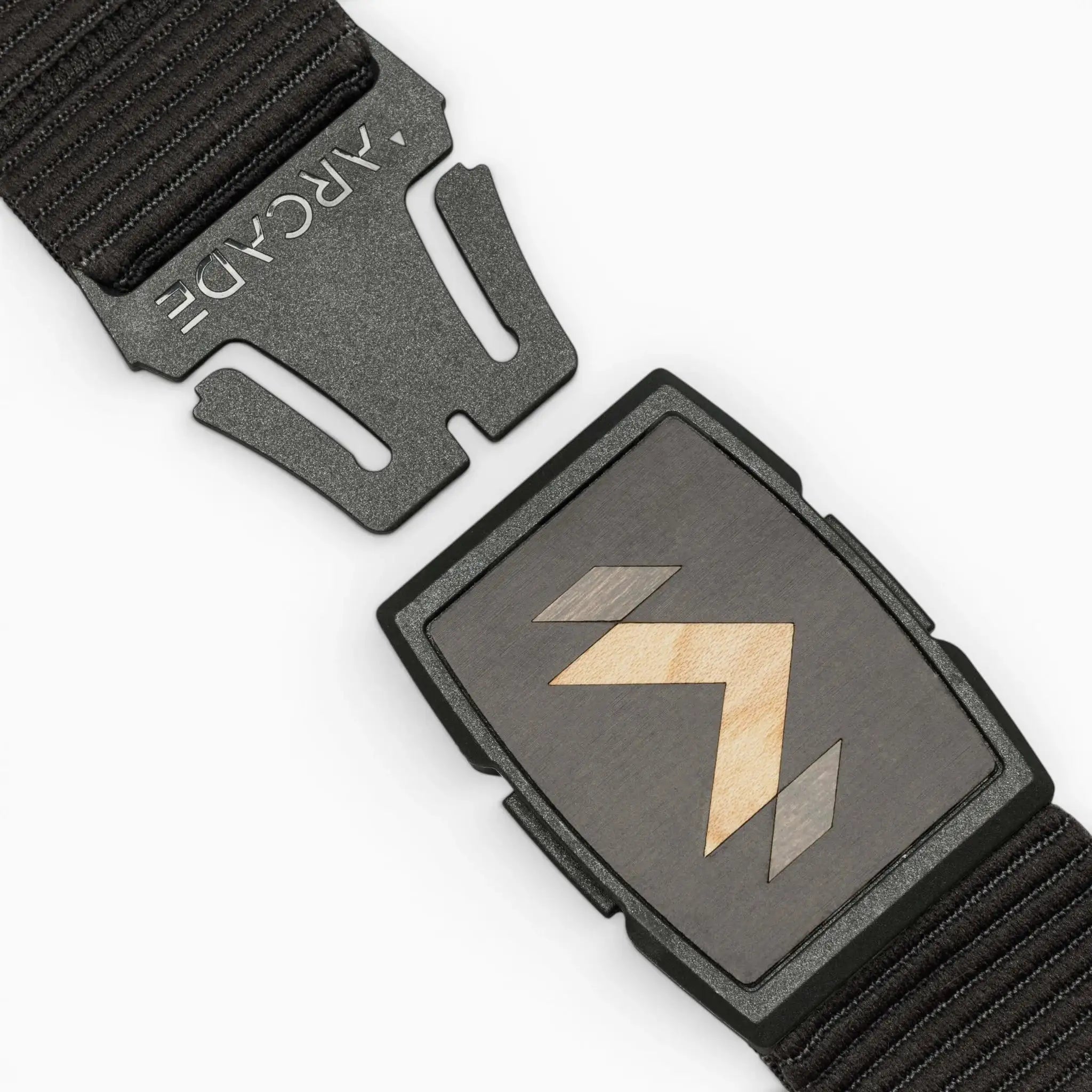 A close-up of the Carver stretch belt by Arcade Belts, featuring a rectangular buckle with a geometric arrow design. The belt is partially unclasped, displaying the ARCADE logo on the clasp.