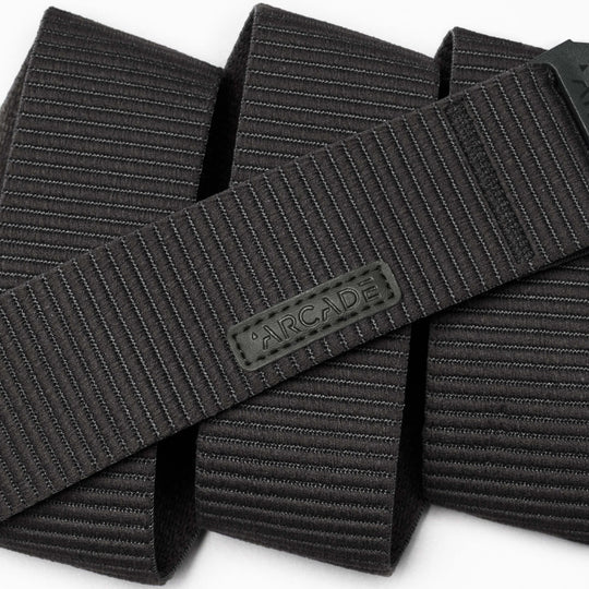 A close-up of the black, textured Carver by Arcade Belts highlights its durable stretch fabric and flexible style, featuring horizontal lines and an ARCADE-branded rubber label.