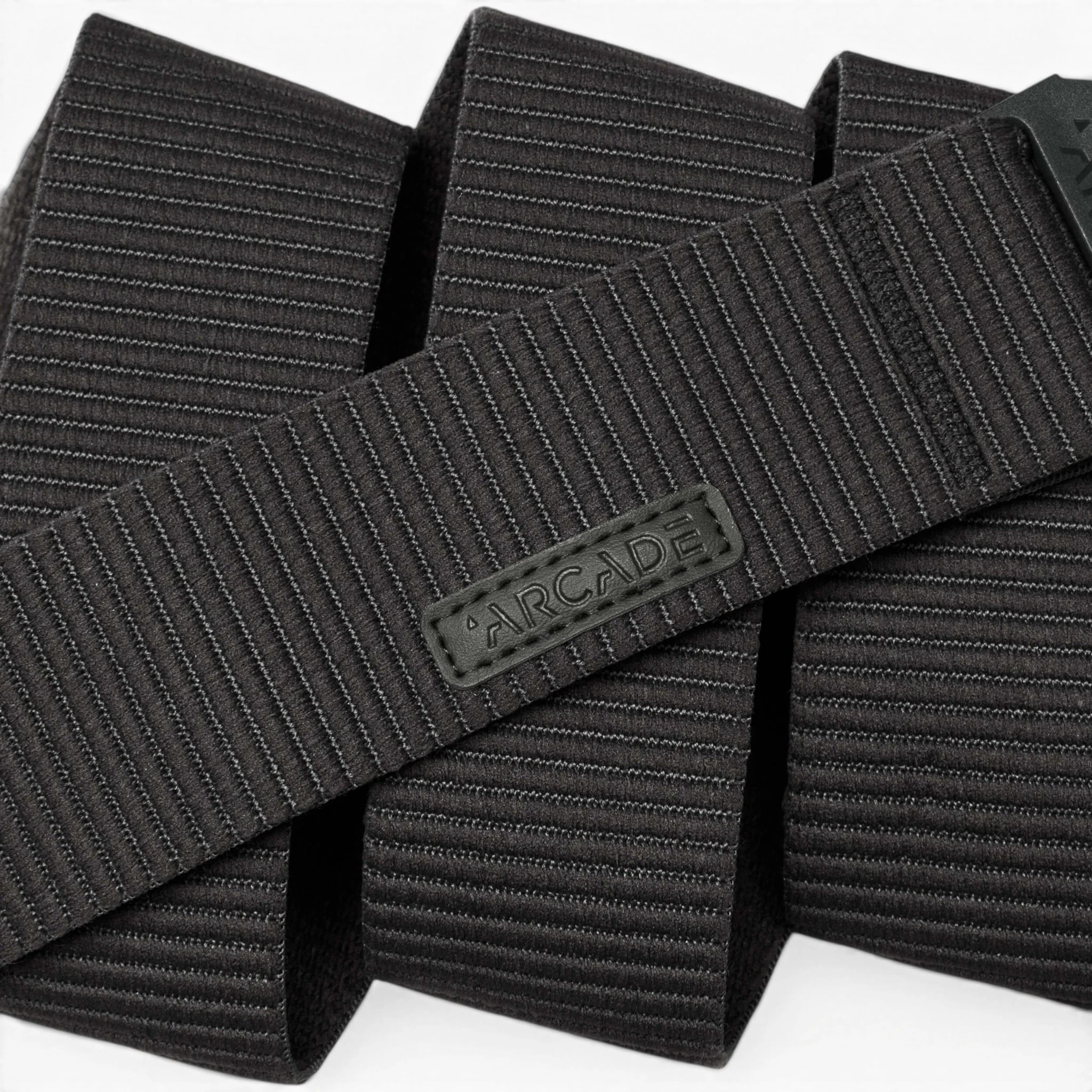 A close-up of the black, textured Carver by Arcade Belts highlights its durable stretch fabric and flexible style, featuring horizontal lines and an ARCADE-branded rubber label.