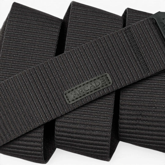A close-up of the black, textured Carver by Arcade Belts highlights its durable stretch fabric and flexible style, featuring horizontal lines and an ARCADE-branded rubber label.