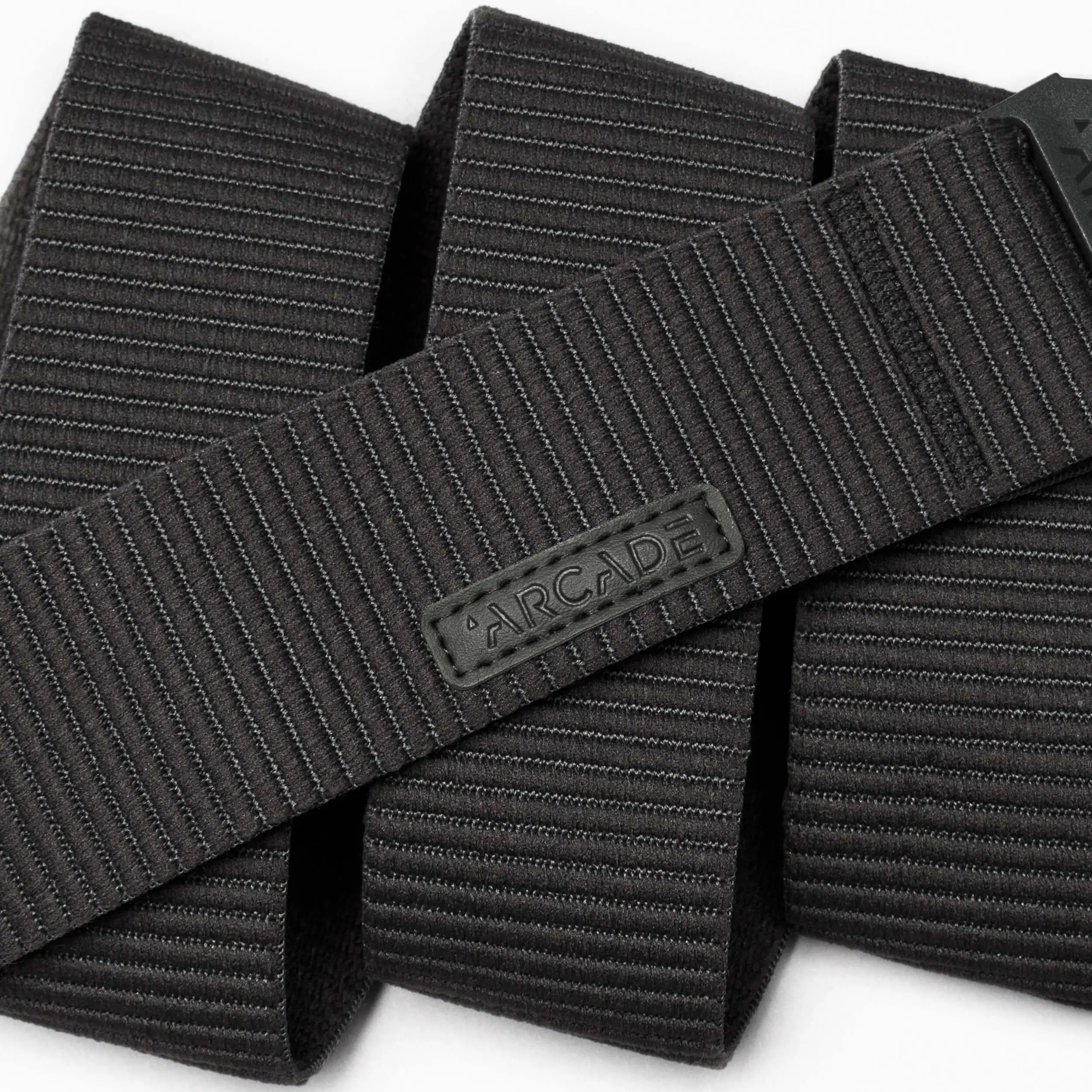 A close-up of the black, textured Carver by Arcade Belts highlights its durable stretch fabric and flexible style, featuring horizontal lines and an ARCADE-branded rubber label.