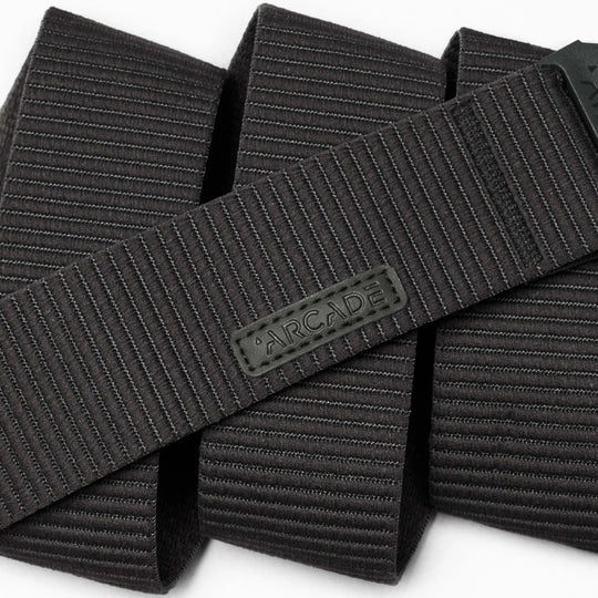 A close-up of the black, textured Carver by Arcade Belts highlights its durable stretch fabric and flexible style, featuring horizontal lines and an ARCADE-branded rubber label.