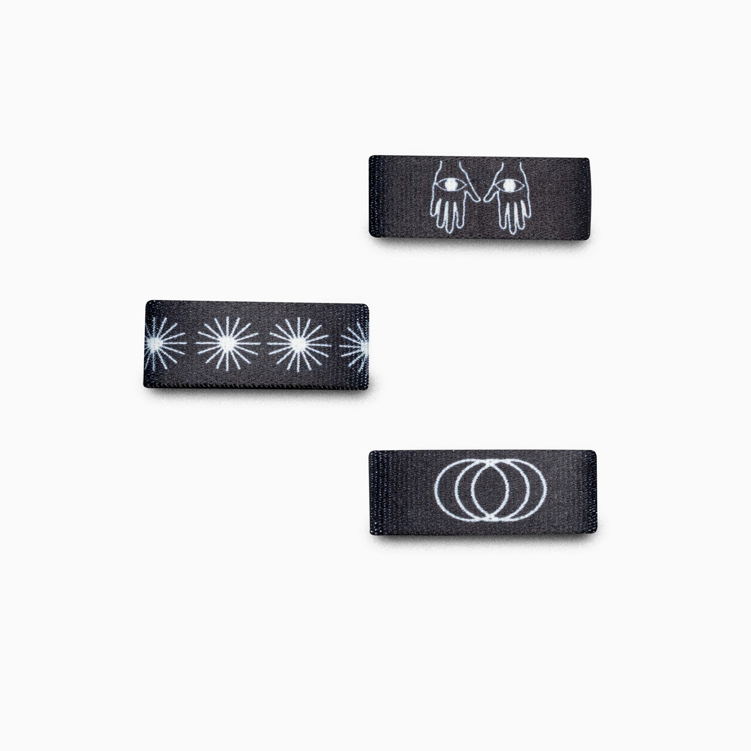 Three Charmer Belt Loopkeepers by Arcade Belts, in black with white designs of hands, starbursts, and overlapping rings—ideal for Lifestyle or Standard Width Adventure Belts—are neatly displayed on a white background.