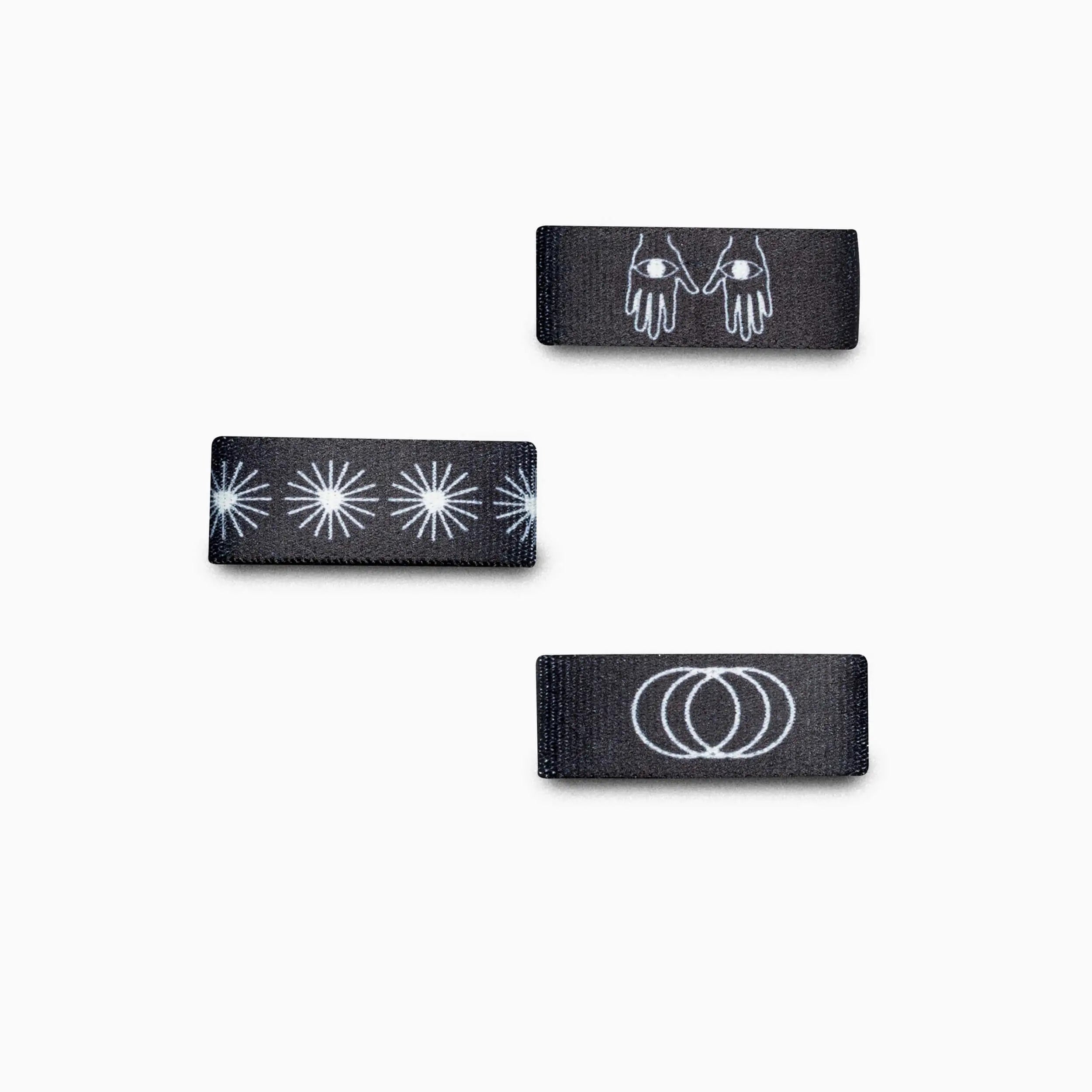 Three Charmer Belt Loopkeepers by Arcade Belts, in black with white designs of hands, starbursts, and overlapping rings—ideal for Lifestyle or Standard Width Adventure Belts—are neatly displayed on a white background.
