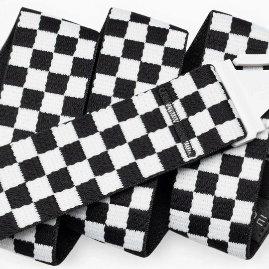 A close-up of the Arcade Belts Check strap shows its black-and-white checkered design and silver buckle. The performance stretch belt is folded and layered against a white background, emphasizing its comfort and flexibility for movement.