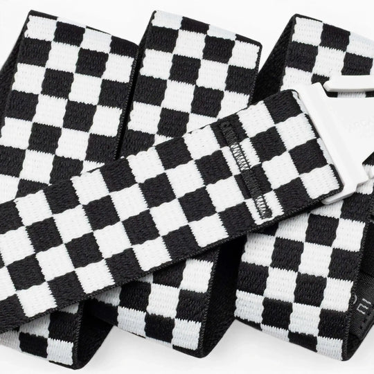 A close-up of the Arcade Belts Check strap shows its black-and-white checkered design and silver buckle. The performance stretch belt is folded and layered against a white background, emphasizing its comfort and flexibility for movement.
