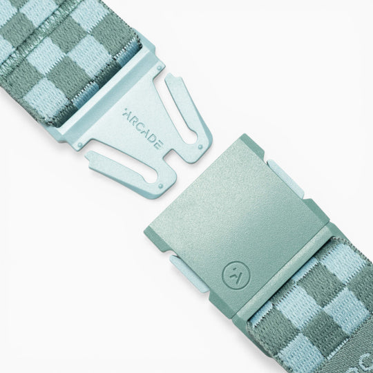 Close-up of the Arcade Belts Check, a blue checkered belt with a metal clasp labelled ARCADE, displayed with its two ends slightly apart on a white background. Designed for performance stretch and made for movement, this stylish accessory from Arcade Belts turns heads wherever you go.