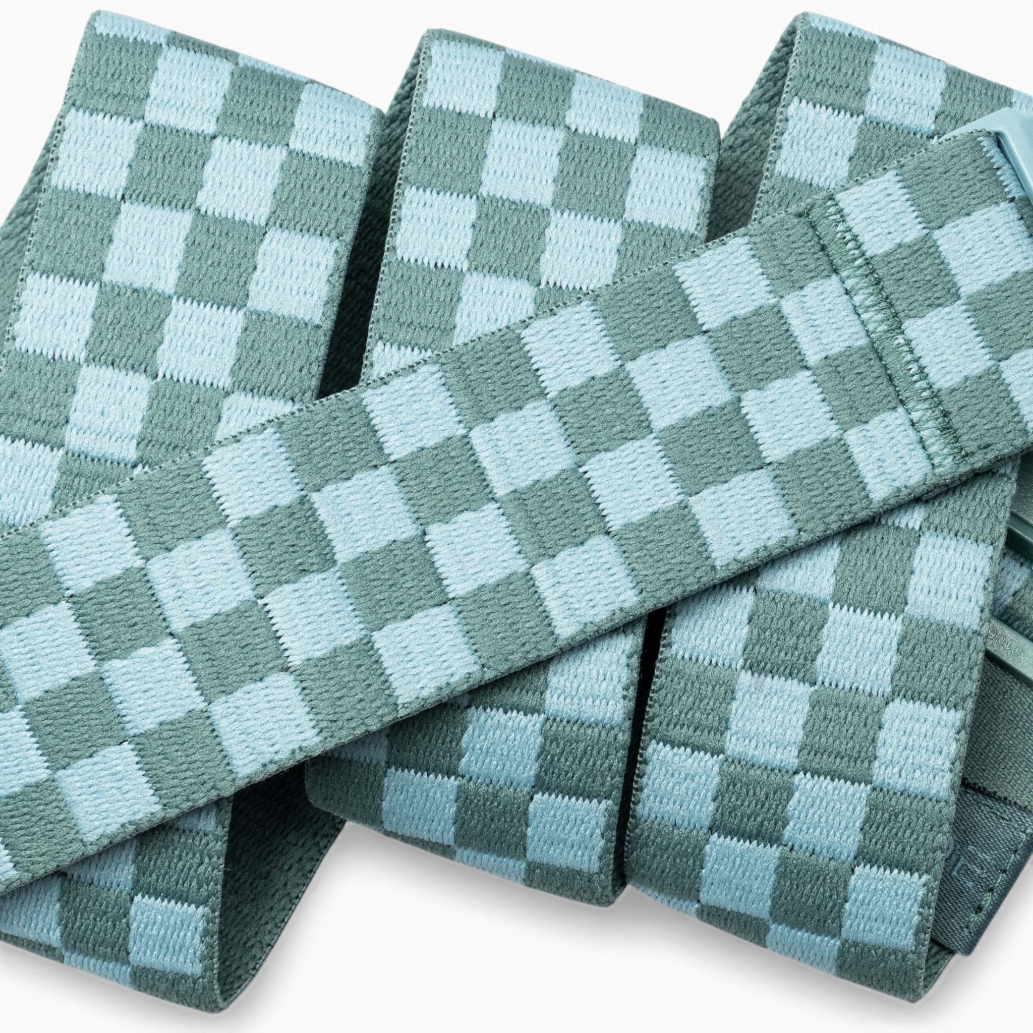 A close-up of the Check belts by Arcade Belts, featuring light blue and teal woven bands in a checkerboard pattern, stacked and overlapping—crafted with performance stretch for flexibility made for movement.
