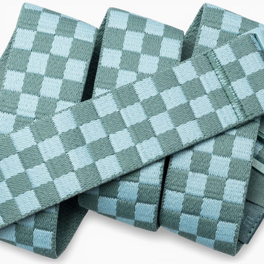 A close-up of the Check belts by Arcade Belts, featuring light blue and teal woven bands in a checkerboard pattern, stacked and overlapping—crafted with performance stretch for flexibility made for movement.